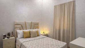 Un dormitorio con cama, mesita de noche, lámpara y cortinas.