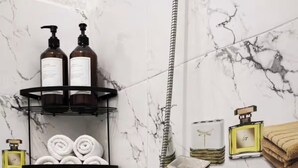 Baño con ducha, azulejos de mármol, toallero con botellas y una toalla colgando.