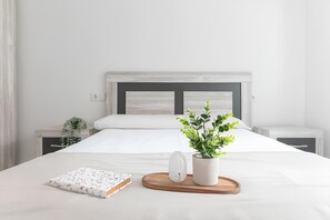 A neatly made bed with white bedding, a bedside table with a plant, a small vase, and a book on a wooden tray. - Modern apartment - private parking - close to beaches (Santander)