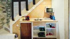 Ett kompakt kök med mikrovågsugn, kaffebryggare och hyllor med tallrikar och köksredskap.
