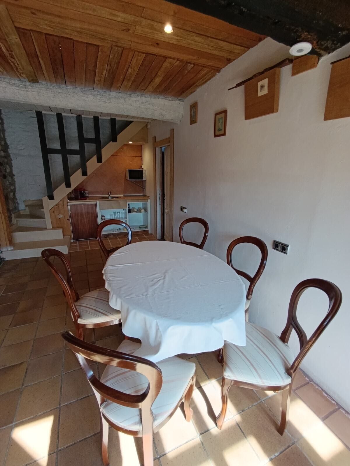 A dining area with a round table and six chairs, a staircase, and a kitchen area.