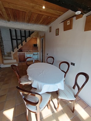 A dining area with a round table and six chairs, a staircase, and a kitchen area.