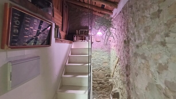 Una stretta scala conduce a un soffitto in legno, con una parete in pietra da un lato e una mensola con diversi oggetti dall'altro.