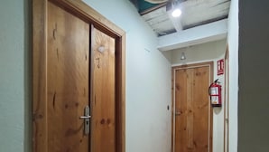 Un corridoio con porte in legno, un estintore e una plafoniera.