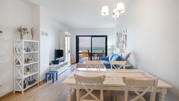 A modern living room with a dining area, white furniture, a TV, and a view of the sea. - Apartment 'Sa Calma I - 1A' with Sea View, Wi-Fi and Air Conditioning (Begur)