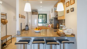 A modern kitchen with a central island, bar stools, a bowl of fruit, and various kitchen appliances. - Apartment 'Sa Calma I - 1A' with Sea View, Wi-Fi and Air Conditioning (Begur)