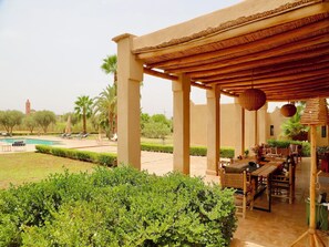 A covered outdoor seating area with a pool, palm trees, and a clear view of a distant tower.