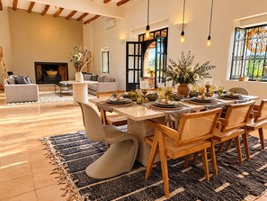 A dining area with a table set for six, surrounded by wooden chairs, a fireplace, and a view of the outdoors.