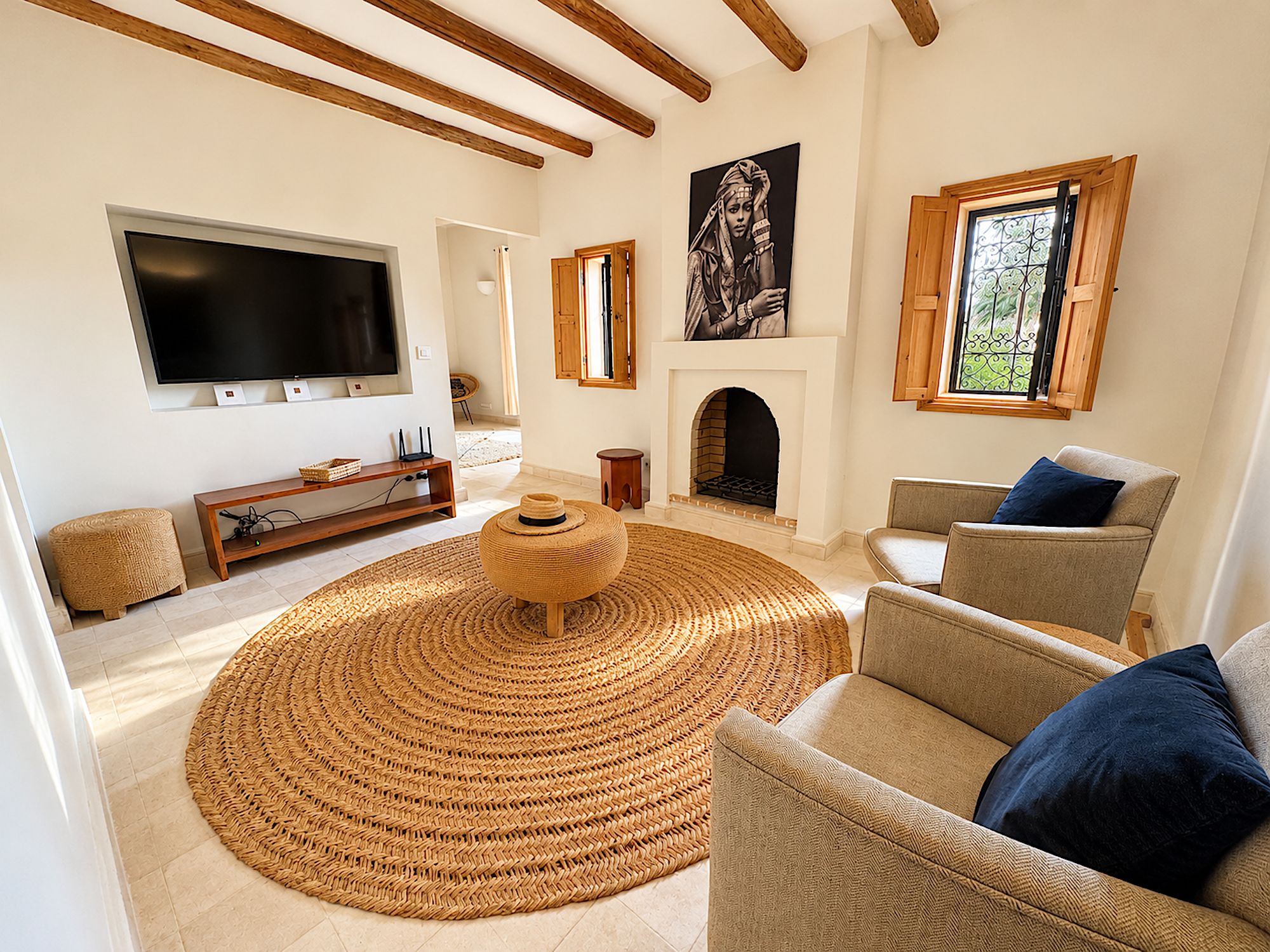 A living room with a large TV, a fireplace, and a round woven rug.