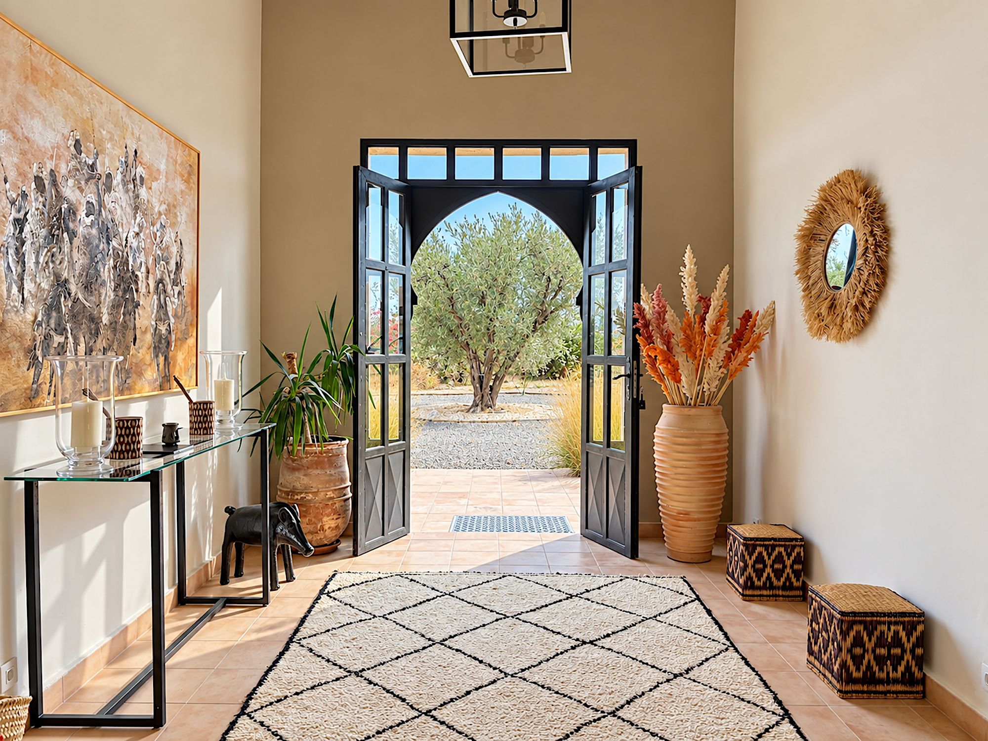 A hallway with a large painting, a glass table with candles, potted plants, a rug, and a large mirror on the wall.