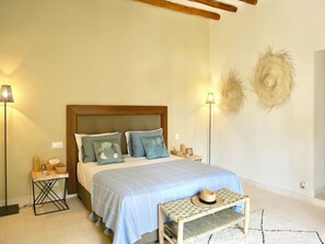 Un dormitorio con cama, mesitas de noche, una silla de mimbre y decoración en la pared.