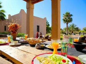 Un área de comedor al aire libre con una mesa lista para el desayuno, incluyendo pan, huevos y fruta.