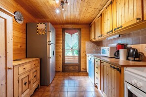 Une cuisine rustique, située dans une cabane en bois, équipée d’un réfrigérateur, d’un four à micro-ondes, d’une cuisinière et de meubles de rangement en bois.