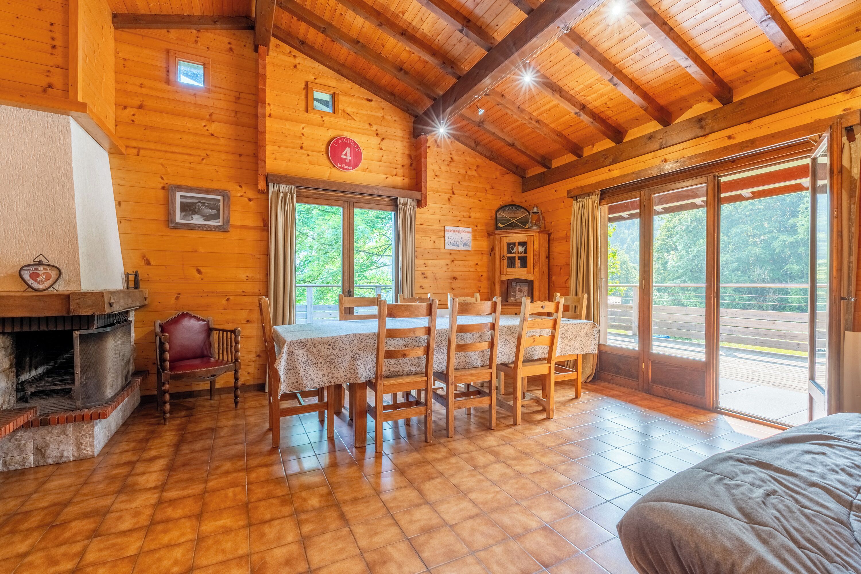 L’intérieur d’un chalet en bois comprend une table à manger, des chaises, une cheminée et de grandes fenêtres.