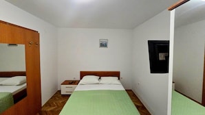 Una habitación con cama, mesita de noche, espejo y un cuadro pequeño en la pared.