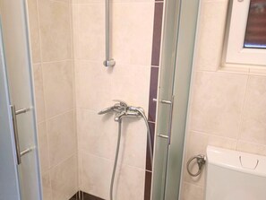 Un angolo doccia con porta in vetro, soffione a mano e rubinetto a parete.