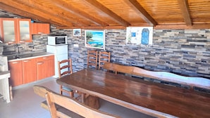 Techo de madera, cocina con microondas, pared de piedra y mesa de comedor con sillas.