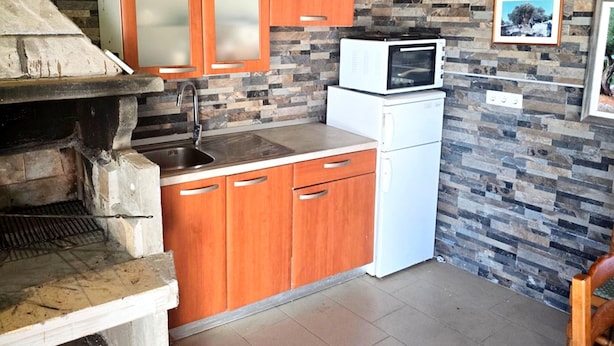 Una cocina con salpicadero de piedra, armarios de madera, horno empotrado, microondas y lavabo.