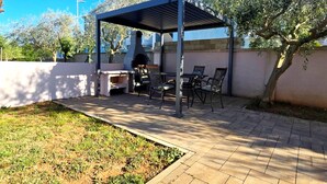Un patio al aire libre con una parrilla, sillas y una pérgola.
