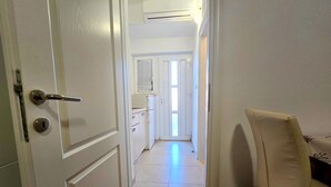Un pasillo con una puerta blanca, una silla blanca y suelo de baldosas.