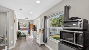 A modern kitchen with a built-in oven and microwave, a green chair, and a view of the outdoors. - Cozy Beach Studio • Walk to the Sand (Pompano Beach)