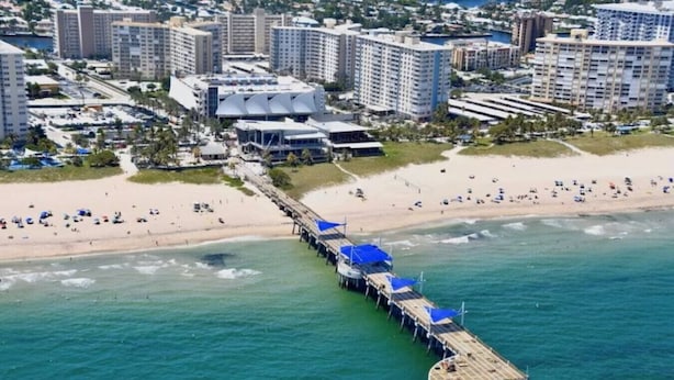 An aerial view of a beach with a pier extending into the ocean, surrounded by high-rise buildings and a sandy shore. - Cozy Beach Studio • Walk to the Sand (Pompano Beach)