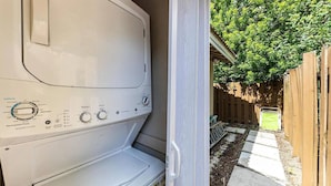 A front-loading washer with control knobs, a wooden fence, and a stone pathway in the background. - Cozy Beach Studio • Walk to the Sand (Pompano Beach)