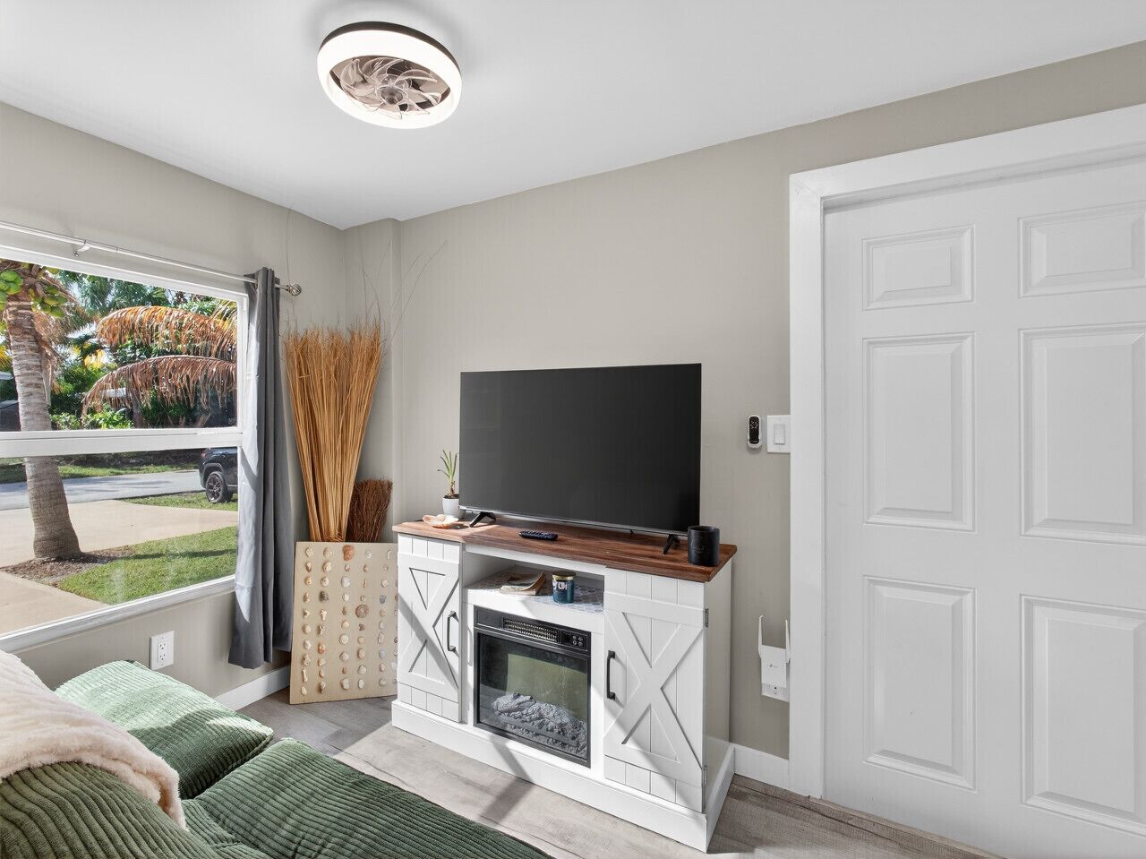 A modern living room with a TV on a wooden cabinet, a fireplace, and a view of a garden.