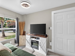 Ein modernes Wohnzimmer mit Fernseher auf einem Holzkasten, einem Kamin und Blick auf einen Garten.