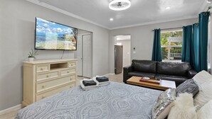 Une chambre à coucher avec un lit, une télévision, une commode, un canapé et une fenêtre avec des rideaux.