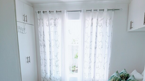 A bedroom with a bed, curtains, pillows, and a view of greenery outside. - Room-charming Guest Room With Private Fa (Gqeberha)