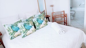 A bedroom with a bed, pillows, a wooden chair, a towel rack, and a view of a bathroom. - Room-charming Guest Room With Private Fa (Gqeberha)