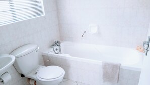 A bathroom with a toilet, sink, bathtub, and a window with blinds. - Room-charming Guest Room With Private Fa (Gqeberha)