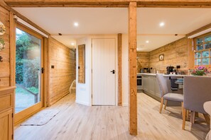A wooden interior with a kitchen, dining area, and a door leading to a garden. - The Parsonage Barns by Keepers Cottages (Preston)