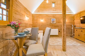 A wooden interior with a dining table, chairs, a small kitchen area, and a window. - The Parsonage Barns by Keepers Cottages (Preston)