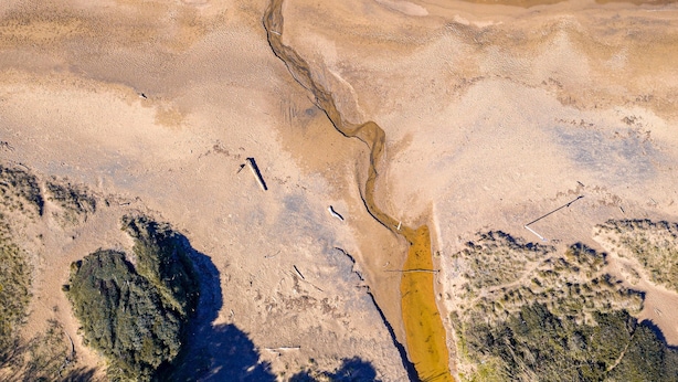An aerial view of a coastal landscape with clear water, sandy areas, and a narrow water channel. - Acqua Shanti Apartment (Piombino)
