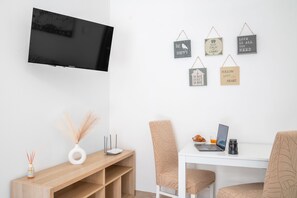 Una camera moderna con TV a schermo piatto, una scrivania in legno, due sedie, un portatile, una tazza di caffè e decorazioni murali motivazionali.
