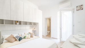 A bedroom with a bed, bedside tables, a wardrobe, and a bathroom visible through an open door. - Acqua Shanti Apartment (Piombino)
