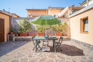 Una terrazza con tavolo e sedie, un ombrellone, piante in vaso e pavimento in pietra.