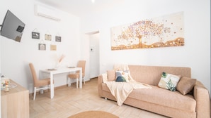 A modern living room with a white desk, a beige sofa, and a large abstract painting. - Acqua Shanti Apartment (Piombino)