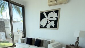 Una sala moderna con un sofá blanco, una mesa de centro de madera, un ventilador de techo y una obra de arte enmarcada en la pared.