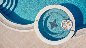 Une piscine circulaire ornée d’une mosaïque en forme d’étoile, une terrasse carrelée et un transat avec un plateau de collations.