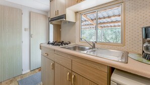 Eine kleine Küche mit Holzschränken, einem Gasherd, einem Spülbecken und einem Fenster mit Blick auf Grünflächen.