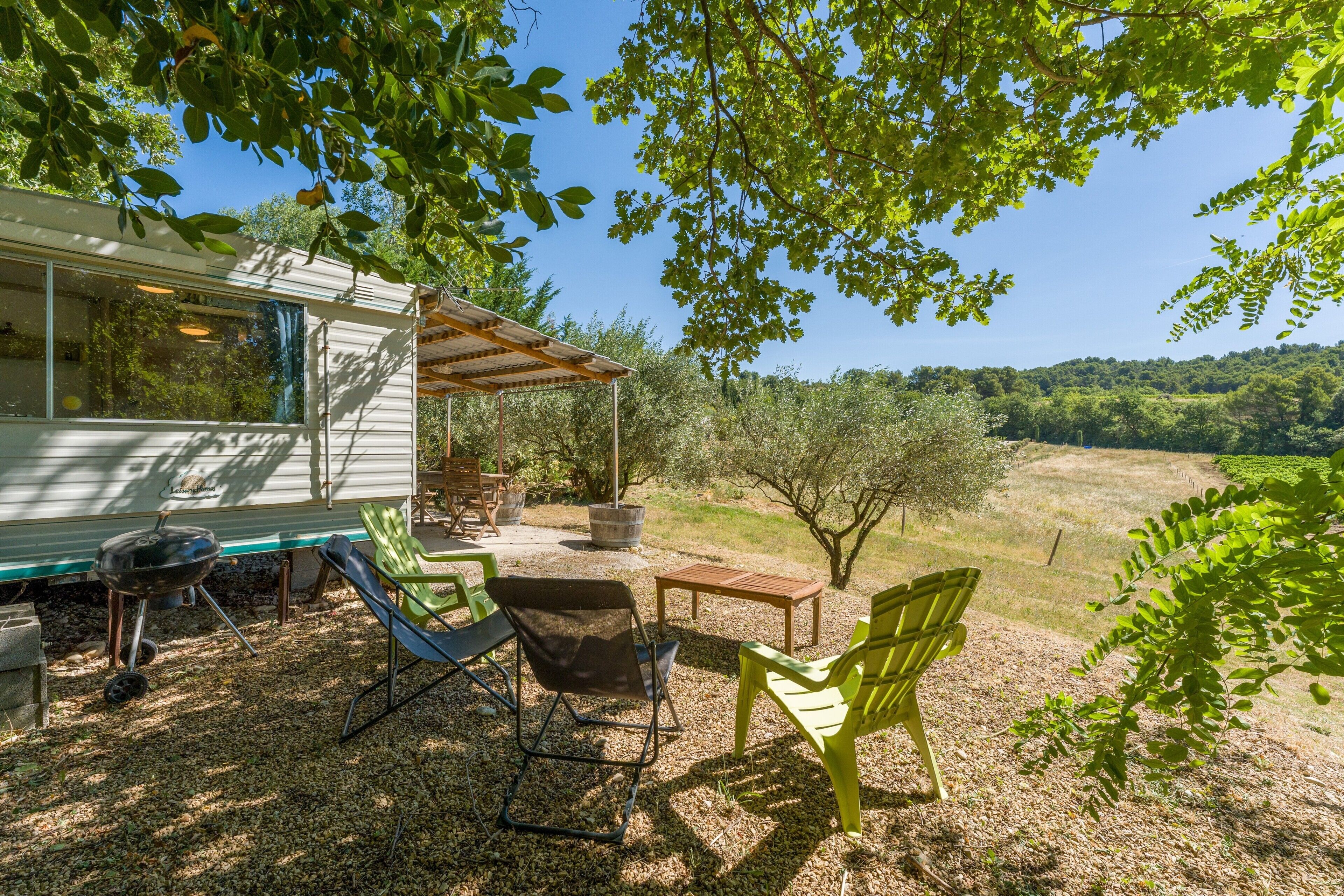 A covered outdoor seating area with chairs and a table, a barbecue grill, and a house with a patio.