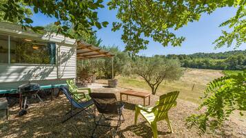 A covered outdoor seating area with chairs and a table, a barbecue grill, and a house with a patio.