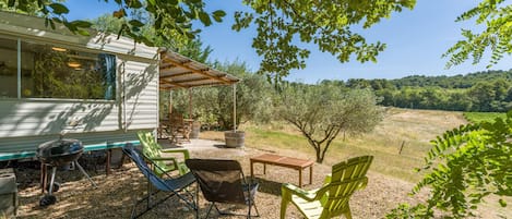 A covered outdoor seating area with chairs and a table, a barbecue grill, and a house with a patio.