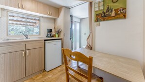 Eine kleine Küche mit Holzschränken, einem Kühlschrank, einem Esstisch mit einem Stuhl und einem Bild an der Wand.