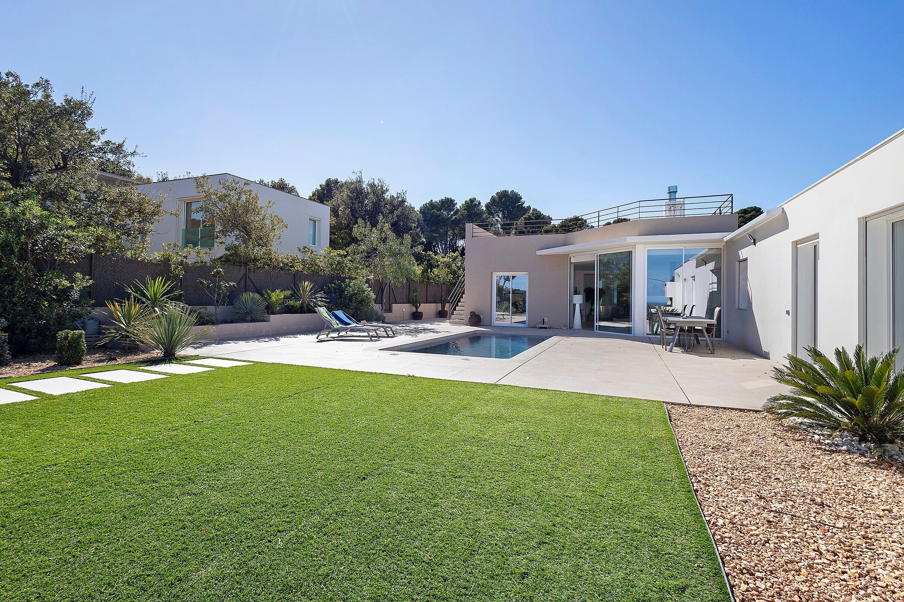 A modern house with a swimming pool, a patio with lounge chairs, and a well-maintained lawn.