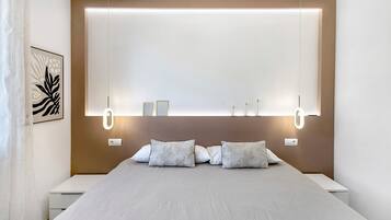 A modern bedroom with a large bed, bedside tables, and wall-mounted lighting.