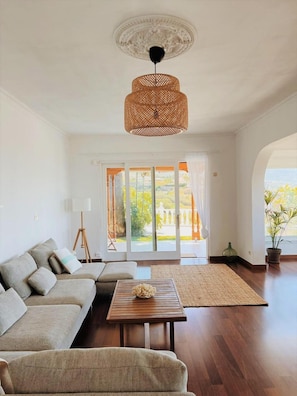 Ein geräumiges Wohnzimmer mit einer großen Couch, einem Holztisch und einer gewebten Pendelleuchte.